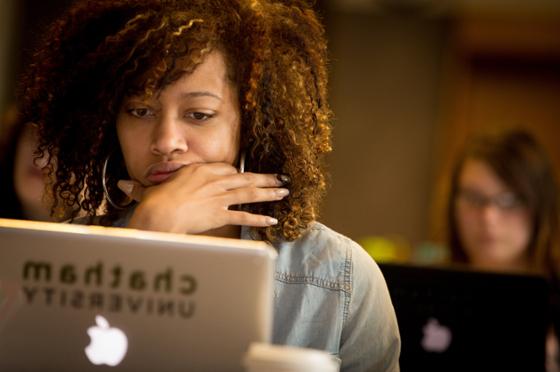 Photo of a student taking notes on a laptop with Chatham University sticker during a lecture. 